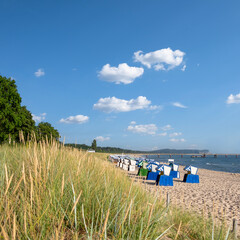 Several beach chairs neatly lined up on a sandy beach overlooking the ocean on a sunny day. Romantic shores of Baltic sea.