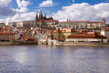 A view of a Prague across a river with castle, St. Vitus cathedral and cityscape of Mala Strana, urban architecture and waterfront scenery.