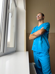 Young doctor in blue clothes looking out the window