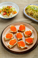 Canapes with red caviar, Thai chicken with rice in sauce, and salad with kiwi on a plate on a wooden table.
