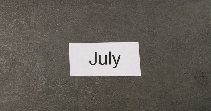 Month names changing on grey table background. Time passing, annual calendar, seasons concept. Top view, 4K stop motion animation.