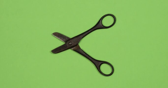 Vintage black scissors in action on green color background. DIY video concept. Top view, 4K stop motion animation loop.