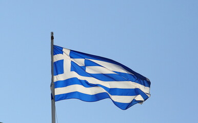 National flag of Greece waves on a flagpole against blue sky