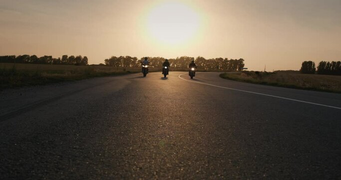 Three bikers drive along the highway past the camera. At sunset. Slow motion shot