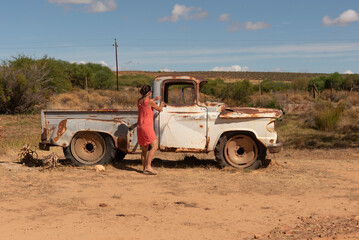 South Africa. 16/02/2024. Attractive woman getting into an old rusty American car on the roadside in the Swartland region of South Africa.