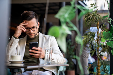 Young serious businessman using a smartphone in a Cafe. Businessman sending a text message to his...