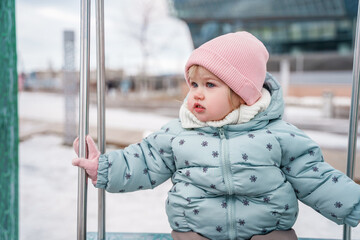 A little girl is a toddler on a swing in the city during the cold season.