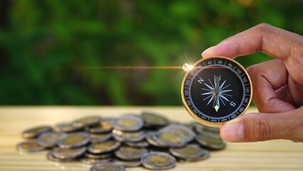 Woman hands hold gold compass with blurred heap of money coins on table with natural background, navigation on money, guideline finance concept. Business Money Learning. Money coach. Travel savings.