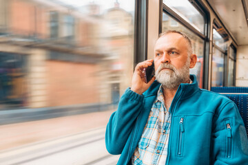 portrait of a bearded man in a blue jacket talking by phone on a bus or tram. Lifestyle concept