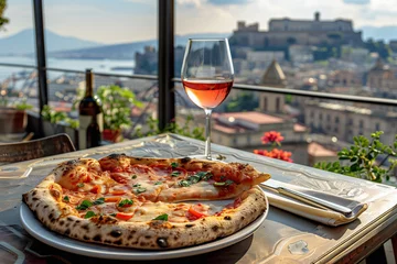 Poster Pizza and a glass of wine on a restaurant table outdoors, with a panorama of Naples in the background © Madeleine Steinbach