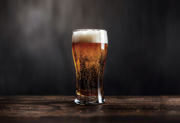 Obraz premium Jarra de vidrio con cerveza y espuma sobre superficie de madera y fondo negro y gris
