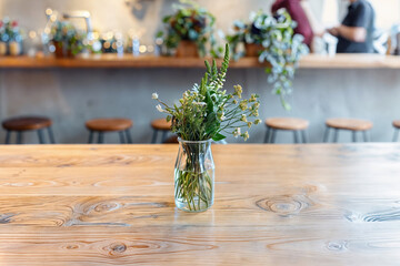 Wildflower arrangement in a transparent vase on a wooden table, with a blurred cafe bar with peoples background.
