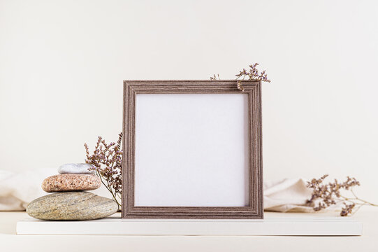 Square empty photo frame surrounded by dried flowers and stones on a light beige background
