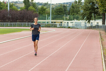 Obraz premium Young woman in sports clothes jogging towards camera on a stadium running track.