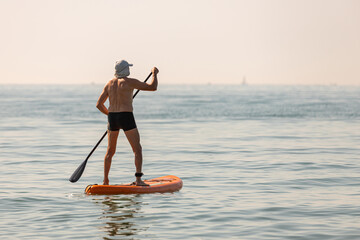 Man standing on a sup board on a calm ocean on a hot summer day during a heatwave; man on a...
