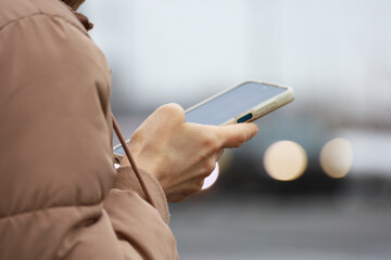 Female hands with smartphone close up on blurred car lights background. Woman using mobile phone on a city street in spring
