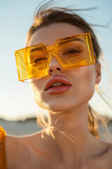 woman with big lips and big yellow geometric sunglasses very fashionable outdoors with back light