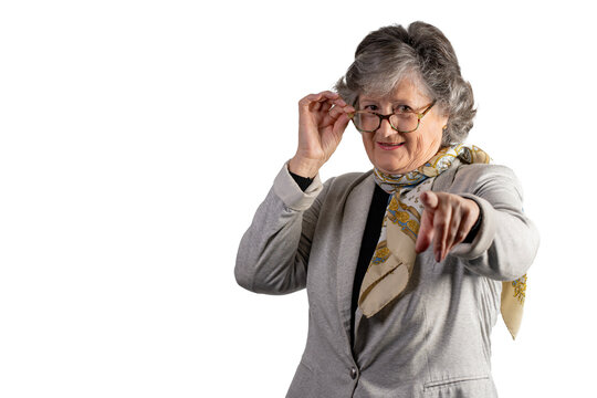 Portrait Of Excited Older Woman Pointing At Something On White Background. Mature Caucasian Woman With Glasses And Gray Jacket Looking At Camera Pointing With Index Finger. Advertising Concept