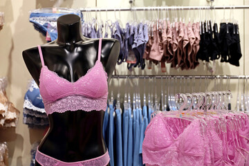 Black female mannequin in pink lace bra and panties. Racks with sexy underwear in lingerie store