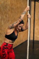 Tired sportive woman climbing a rope in a gym