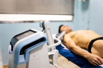 An adult man undergoes super inductive system therapy for recovery from trauma and rheumatic pathologies in a physiotherapy clinic.The machine is in the foreground. Super Inductive System, SIS. - obrazy, fototapety, plakaty