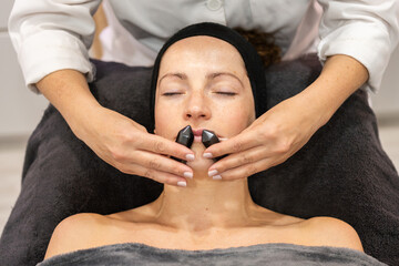 Woman having facial massage with mineral stones in salon
