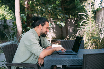 A male freelancer, a digital nomad, remotely works on a laptop in the hotel garden.