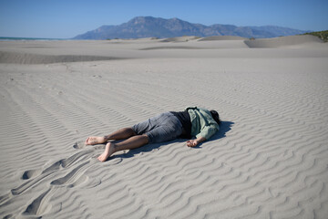 An emaciated man crawls under the scorching sun on the sand in the desert.