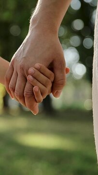 Mother and child holding hands on sunset background. Daughter takes mother's hand in park. Sun flares nature. Concept of family, trust, love and happiness. Vertical video