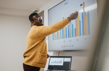 Confident African American businessman giving a presentation with a chart on a whiteboard in a bright office setting.