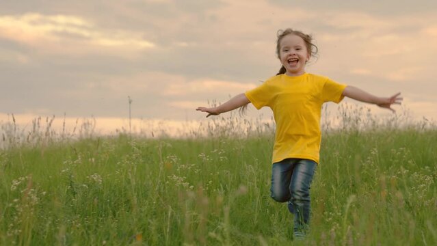 Happy little girl dreams of flying in nature. Children fantasies. Happy child, girl runs raising her hands like flyer in green grass. Child running through field of flowers at sunset. Happy family.