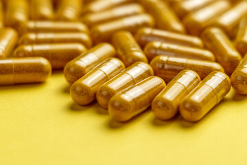 Yellow turmeric (curcuma) supplement capsules on a creative colour background. Herbal medicine pills