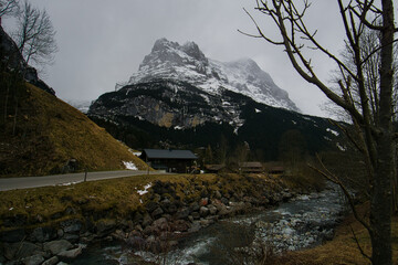 Scenic lodge and creek in front of misty swiss alpine panorama in early spring 