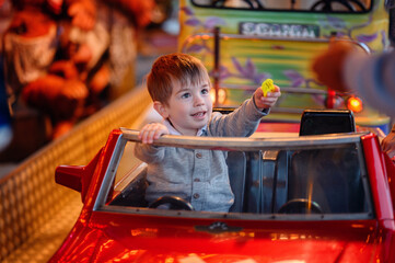 A bright-eyed toddler holds the wheel of a red toy car and gives a ticket token, his imagination...