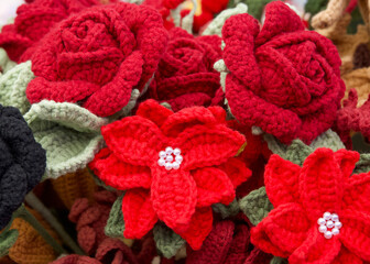 Close up on bouquet of beautiful hand crafted crochet flowers. Red clustered flowers with roses behind.