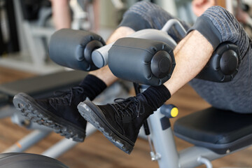 Man using a leg press machine in a well equipped gym. Male legs wearing black sneakers and grey...
