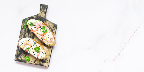 Bruschette set with shrimps, cream cheese, sesam seads and aromatic herbs on rustic wooden serving board top view, copy space for your design.