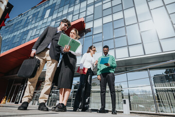 A group of businesspeople are engaged in a meeting outdoors, with the city's modern architecture as their backdrop on a bright sunny day.