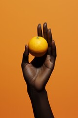 Graceful Balance: Elegant Hand Holding a Single Lemon on Orange Background