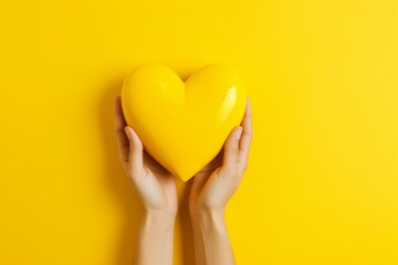 Caring Hands Holding Yellow Heart on Vibrant Yellow Background - obrazy, fototapety, plakaty