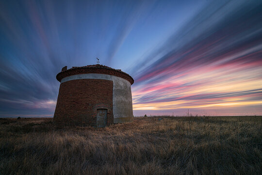 Sunset with intensely colored clouds over the Ledigos dovecote, Tierra de Campos, Palencia in summer with dry grass around