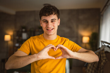 Portrait of one caucasian man 20 years old looking to the camera at home smiling show hand hart...