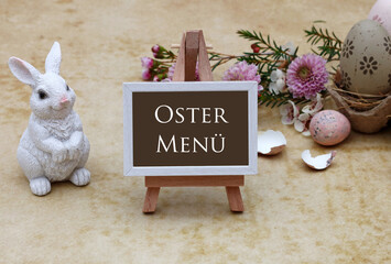 Der Text Ostermenü ist auf eine Tafel geschrieben mit Ostereiern und Blumen geschmückt.