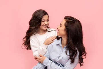 Mother daughter bonding. Pretty girl and her mom hugging and looking to each other, posing on pink...