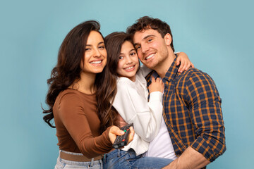 Parents and daughter embracing together posing on blue studio background, smiling at camera. Shot of loving family concept