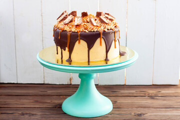 Peanut butter cake with salted caramel, melted chocolate and sweets on green cake stand