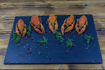 Slate board with boiled crayfishes on a wooden table