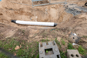 pipeline on construction side. White pipe lies in hole in the ground.