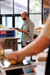 An Arab male customer browsing on the internet while looking at a certain section in an environmentally friendly grocery store. Modern technology being utilized in a sustainable supermarket.