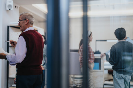 Experienced senior businessman with glasses leading a strategic meeting with diverse team in a contemporary office setting. - Powered by Adobe